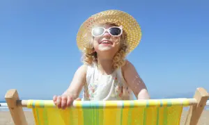 Bambina sorridente con cappello di paglia e occhiali da sole, seduta su una sdraio. Posso usare la crema solare per bambini per proteggerla dal sole.