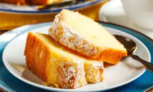 Deux parts de gâteau au yaourt moelleux, saupoudrées de sucre glace, sur une assiette blanche avec une cuillère ornée.