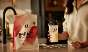 Frau hält Shaker mit gelbem Getränk neben Myprotein Impact Whey Protein. Perfekt für einen protein shake vor dem schlafen.