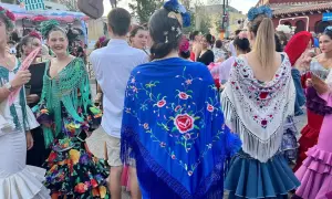 Mujeres con trajes de flamenca y mantones bordados, uno azul con flores rojas y otro blanco con detalles coloridos.