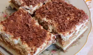 Pyszne ciasto krówka bez pieczenia, warstwowe, z kremem i posypką czekoladową, na ozdobnym talerzyku.