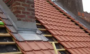 Dachdecker arbeiten am Schornstein, um ihn abzudichten. Neue rote Dachziegel werden verlegt.
