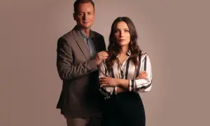 Mężczyzna w garniturze i kobieta w bluzce w paski stoją obok siebie.