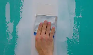 Main d'un artisan ponçant un mur à la main avec une spatule pour lisser le plâtre.