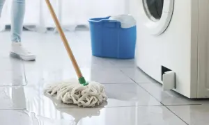 Eine Person wischt Wasser auf, das aus einer Waschmaschine austritt. Ein blauer Eimer steht bereit.
