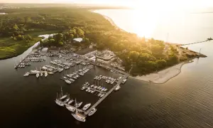 Zachód słońca nad zatoką, gdzie cumują liczne jachty. Widok na górki zachodnie marina, otoczoną zielenią i piaszczystą plażą.