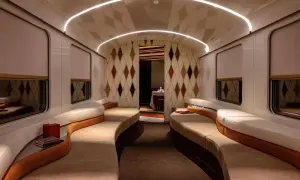 Luxuriöses Interieur eines Nachtzugs nach Italien mit geschwungenen Sofas, Rautenmuster-Tapete und indirekter Beleuchtung.