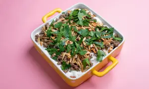 Un plat de fatteh aubergine garni de viande hachée, d'amandes effilées et de persil frais, dans un plat jaune à pois blancs.
