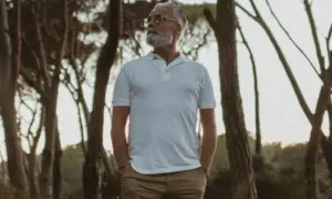 Älterer Mann mit Bart in weißem Polo und brauner Hose, steht im Wald. Die polo farben sind klassisch und zeitlos.
