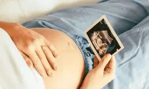 Kobieta trzyma kartę ciąży, patrząc na zdjęcie USG swojego dziecka.