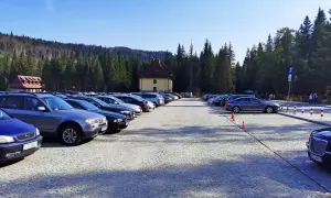 Duży parking przy Palenicy Białczańskiej, pełen samochodów, z górami i lasem w tle.