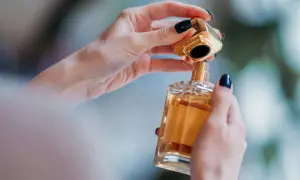 Dłonie z ciemnym lakierem do paznokci otwierają luksusowe perfumy. Złota nakrętka unosi się nad szklaną butelką z bursztynowym płynem, niczym zapowiedź zapachu Nasomatto Black Afgano.