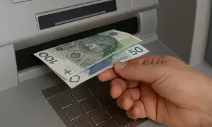 Dłoń wyjmuje banknoty 100 i 50 zł z bankomatu. Czy współwłaściciel konta może wypłacić pieniądze po śmierci właściciela?