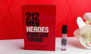 Czerwone opakowanie Carolina Herrera 212 Heroes Forever Young obok atomizera i białych kwiatów.