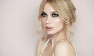 Blondynka z grzywką na boki i prostymi włosami, z błękitnymi oczami i delikatnym makijażem.
