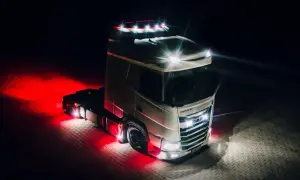 Camion DAF blanc illuminé par des feux de jour et des lumières rouges vives sur un sol pavé la nuit.