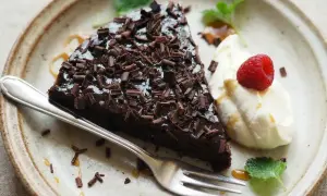 En bit glutenfri kladdkaka med chokladspån, vispad grädde, hallon och mynta på en tallrik.