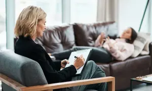 Una psicologa annota su un blocco note mentre una paziente sdraiata sul divano parla. La frequenza con cui si va dallo psicologo varia.