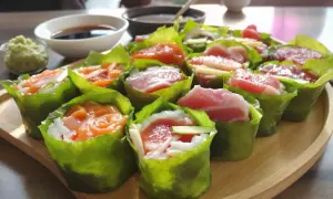 Pyszne sushi w liściach sałaty, z łososiem i tuńczykiem w środku. Obok miseczka z sosem sojowym i wasabi.