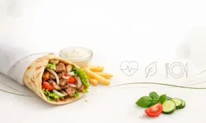 Kebab z mięsem, warzywami i frytkami, obok sos i świeże warzywa.
