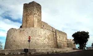 Imponente castello di Monte Sant'Angelo, con mura in pietra grezza e un torrione svettante sotto un cielo nuvoloso.