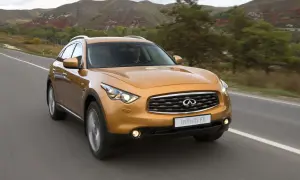 Pomarańczowy Infiniti QX70 jedzie po drodze wśród jesiennych wzgórz.