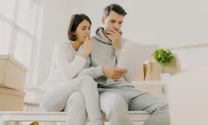 Couple inquiet, entouré de cartons, face à un loyer impayé locataire en détresse. Ils semblent préoccupés par des documents.