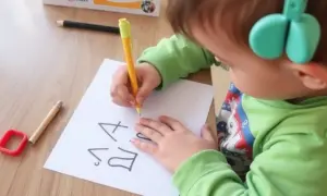 Dziecko z zielonymi słuchawkami ćwiczy pisanie, by pokonać dysgrafię. Na kartce widać litery.