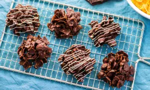 Sei dolcetti croccanti al cioccolato, simili a rose del deserto, raffreddano su una griglia. Alcuni sono decorati con sottili fili di cioccolato bianco.