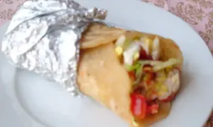 Pyszny kebab w cieście, zawinięty w folię aluminiową, z widocznymi warzywami i mięsem.