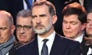Król Hiszpanii Felipe VI w garniturze i krawacie, otoczony przez innych mężczyzn.