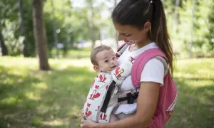Uśmiechnięta mama z dzieckiem w nosidełku dla dziecka z lisami, na tle zielonego parku.