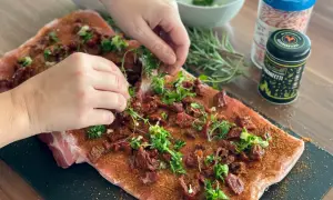 Hände belegen rohes Schweinefleisch mit Kräutern und getrockneten Tomaten für Porchetta.