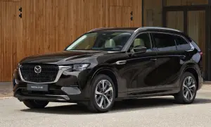 Elegancka, czarna Mazda CX-80 SUV stoi przed nowoczesnym budynkiem z drewnianą elewacją.