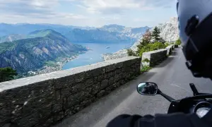 Widok z motocykla na Zatokę Kotorską w Czarnogórze. Kręta droga, kamienny mur i zapierająca dech w piersiach panorama gór i morza.