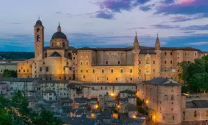 Urbino Natale: il Palazzo Ducale illuminato al crepuscolo, con le sue torri e la cupola, domina la città storica.