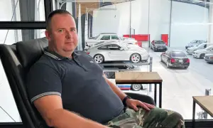 Robert Michalski, w wieku około 40-50 lat, siedzi w czarnym fotelu. W tle widać kolekcję samochodów.
