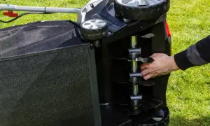 Dłoń dotyka noży wertykulatora na odwróconej maszynie na trawniku.