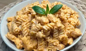 Fusilli conditi con una cremosa salsa al pesto e pomodorini, guarniti con foglie di basilico fresco.