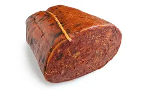 Ein Stück Nduja, eine kalabrische Streichwurst, mit grober Textur und roter Farbe, an einem Faden gebunden.