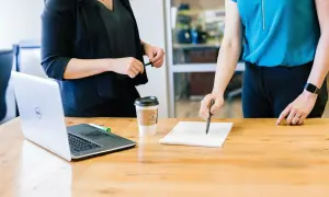 Dwie kobiety omawiają umowę ramową przy biurku z laptopem i kawą.