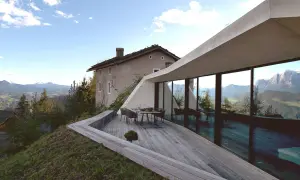 Modernes Haus in Hanglage mit Panoramafenstern und Terrasse, daneben ein altes Bauernhaus, umgeben von Berglandschaft.