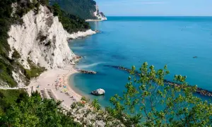 Spiaggia dei frati con scogliere bianche, mare azzurro e alberi verdi.