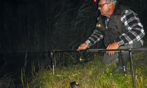 Ein Angler mit Stirnlampe prüft nachts seine John Sidley Rig-Ausrüstung am Ufer.