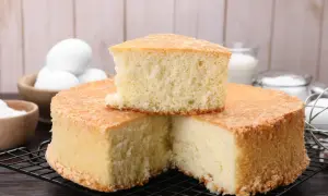 Puszysty biszkopt na kratce, obok miseczki z jajkami i cukrem.