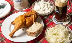 Knusprige Henne Berlin mit Brot, Krautsalat und einem Bierkrug.