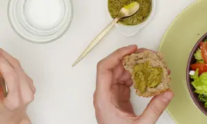 Main d'une personne tenant un morceau de pain avec du pesto, à côté d'une salade.