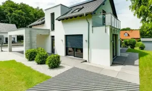 Nowoczesna, biała elewacja domu z panelami słonecznymi na dachu, przeszklonym balkonem i minimalistycznym ogrodem.