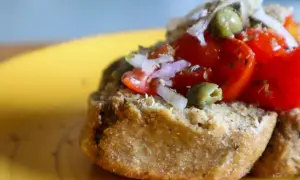 Una gustosa frisa pugliese condita con pomodorini, cipolla rossa e olive verdi, su un piatto giallo.