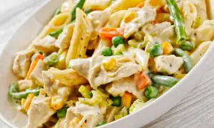 Pyszny kurczak z makaronem penne, groszkiem, marchewką i fasolką szparagową w kremowym sosie.